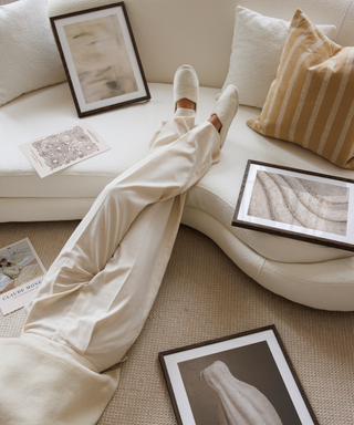 A pair of crossed legs in a neutral living room surrounded by beige art prints