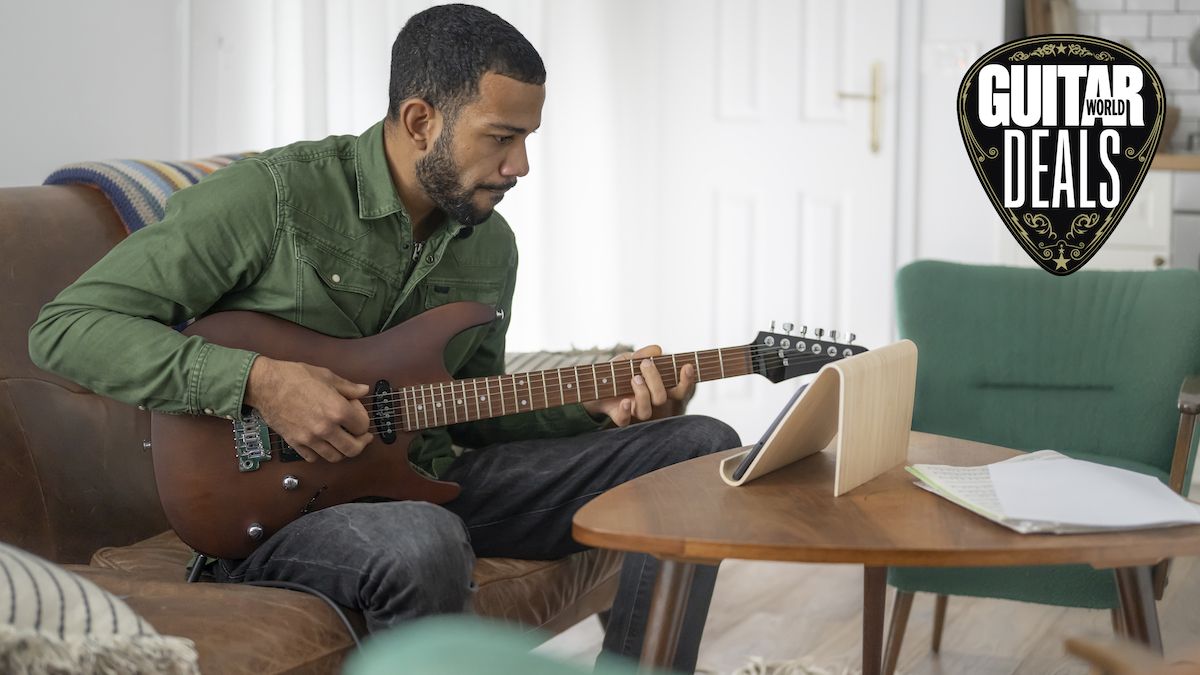 Man playing brown guitar watches a guitar lesson on his tablet