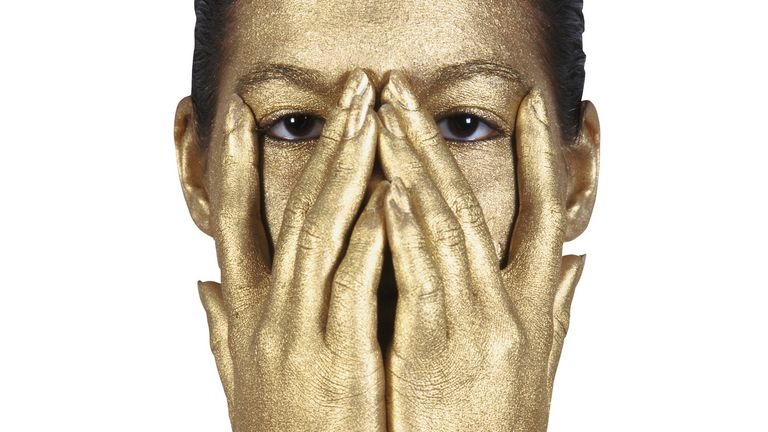 Woman's face and hands covered in gold body paint