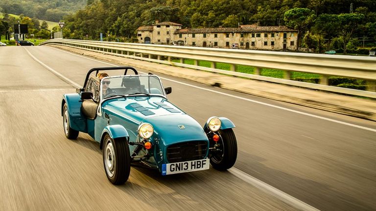 A blue Caterham Seven, one of the best kit cars, being driven along a road