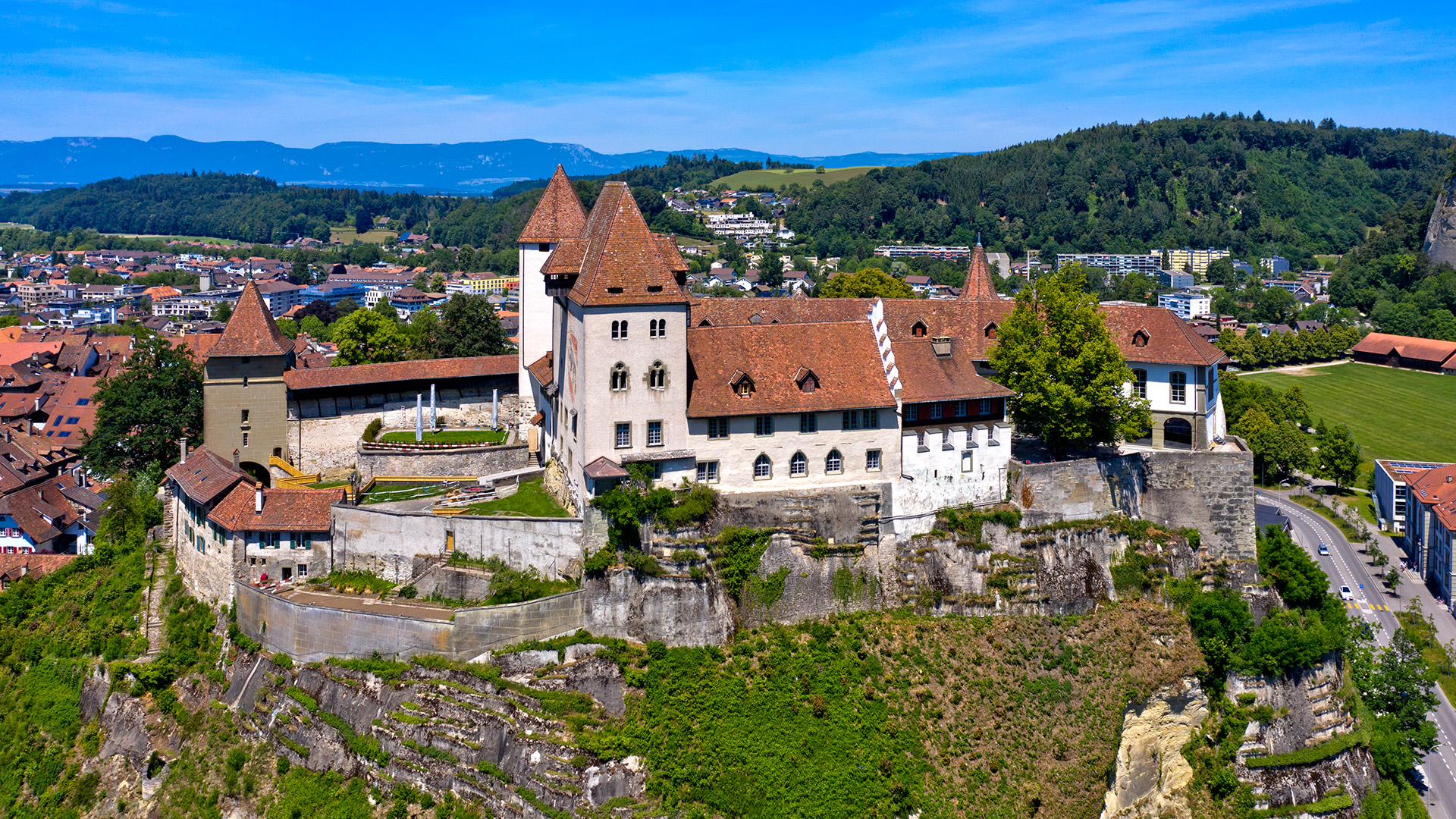 An aerial view of a large white castle with red brick roofs and a series of stone walls around the buildings.