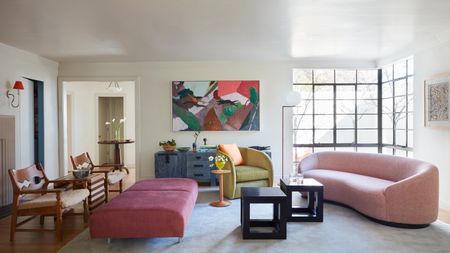 Image of a white living room with a curved pink sofa and matching accent chair in lime green.There are two small black coffee tables in front of the sofa and a long dark pink ottoman