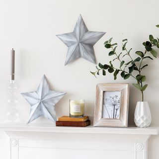 Silver stars wall art above a fireplace on a white wall with a candle, frame and vase