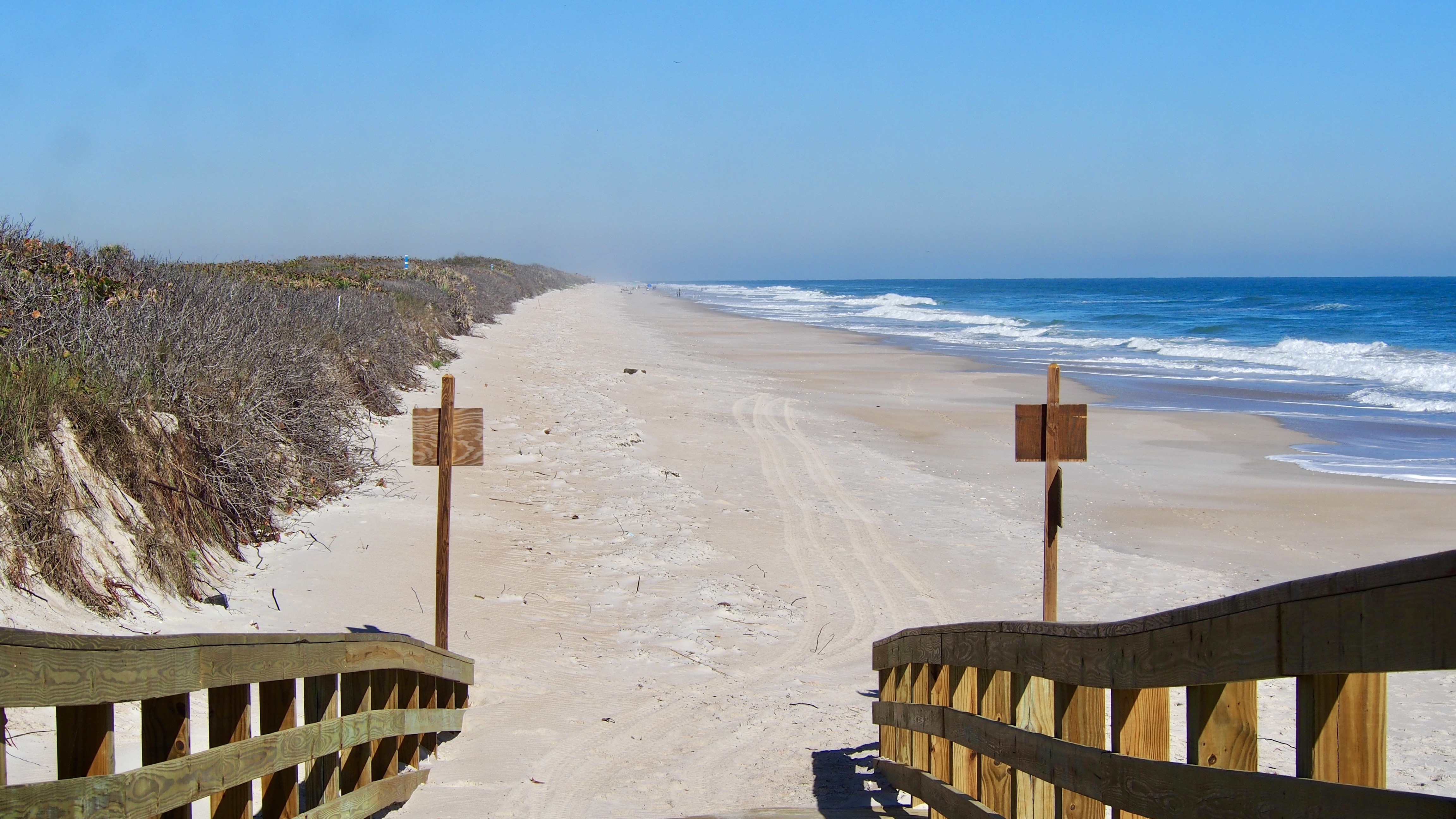 wooden handrails slope down to a long empty beach.