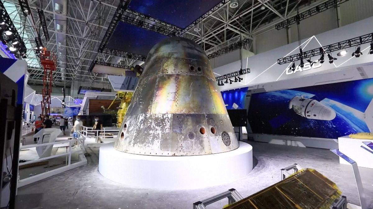 a silver space capsule sits in a museum surrounded by other pieces of space hardware