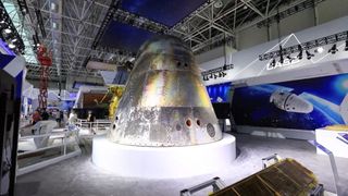 a silver space capsule sits in a museum surrounded by other pieces of space hardware