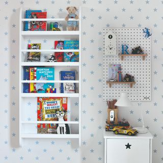 A children's playroom covered in a star wallpaper with a wall-mounted bookshelf, a peg board used as display and a small cabinet