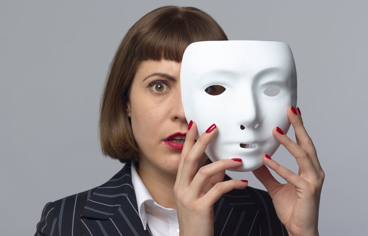 businesswoman whose face is half-covered by a white mask she&#039;s removing