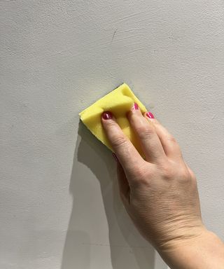 Womans hand with yellow sponge washing wall
