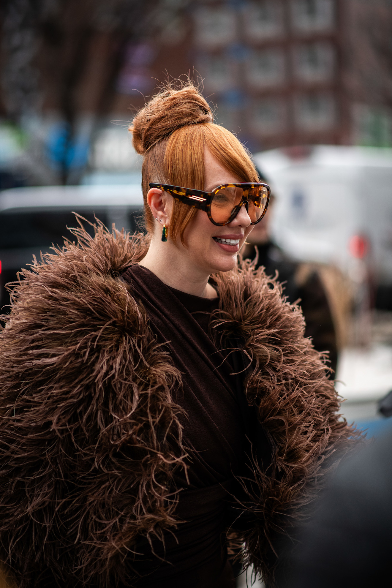 a woman with red hair in a top know bun in a brown fuzzy jacket and sunglasses