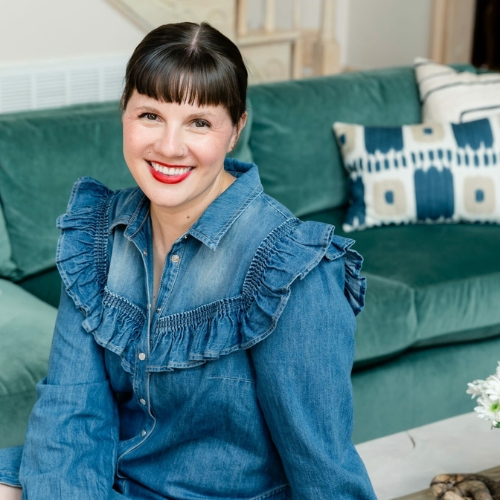 Image of a woman wearing a ruffled denim dress sitting in front of a teal sofa.