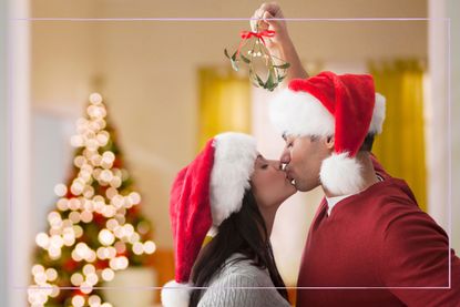 A couple kissing under the mistletoe while wearing Santa hats