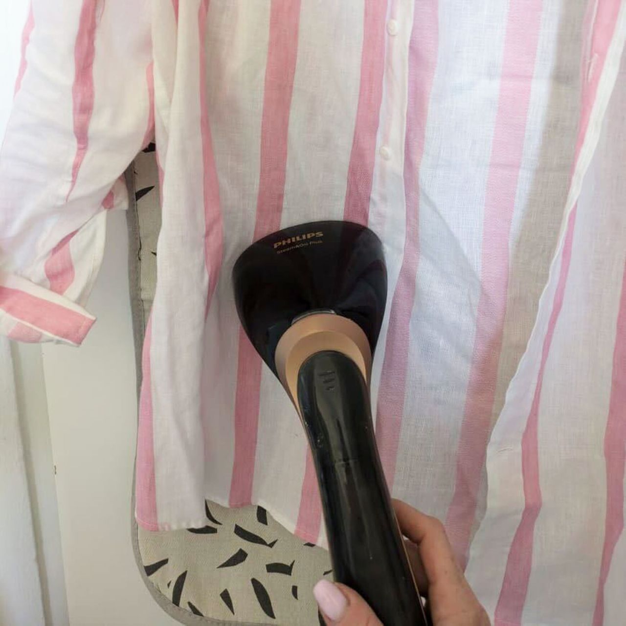 Pink and white striped shirt being steamed in front of ironing mat