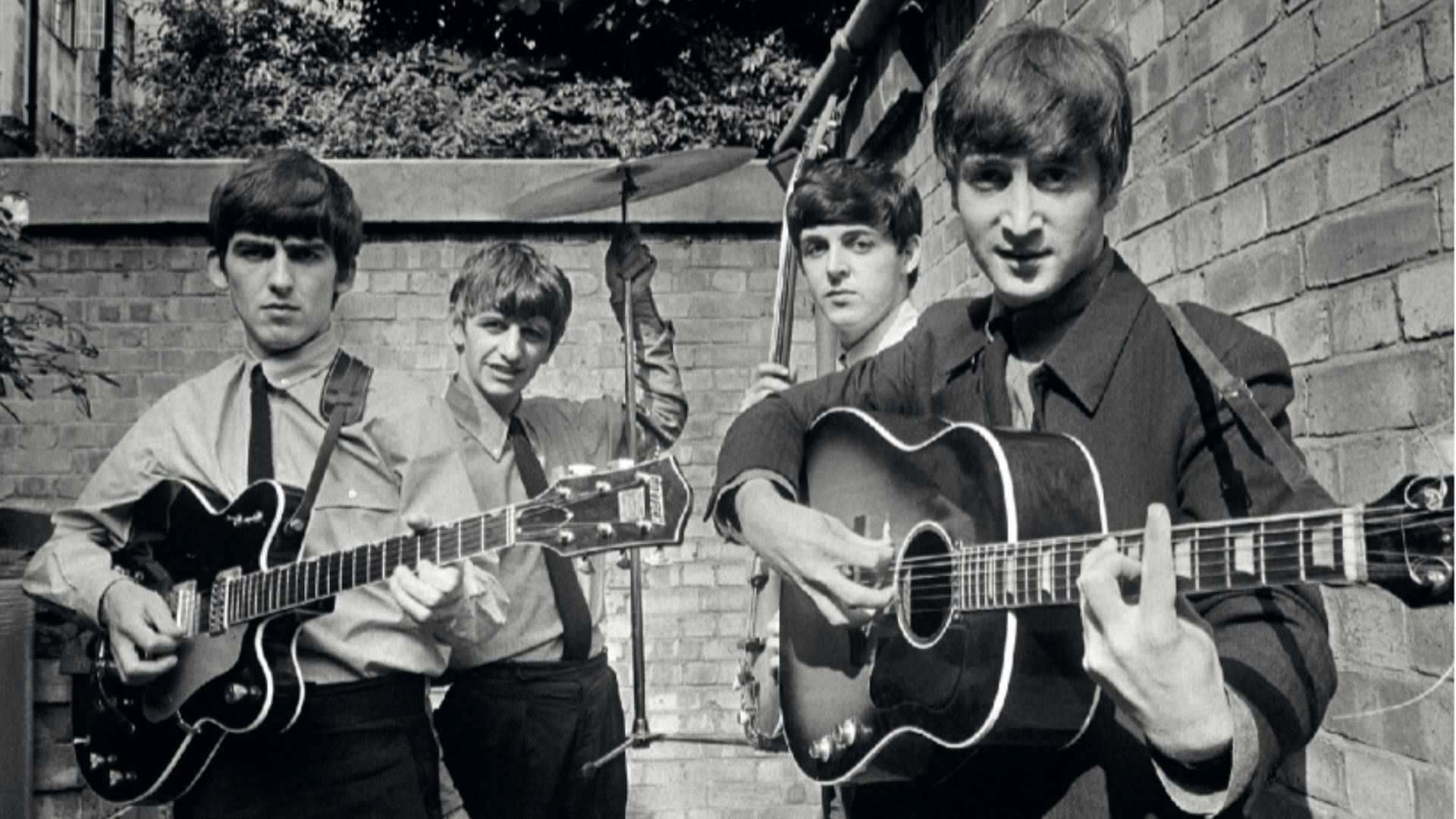 a black and white image taken by Terry O Neill showing the four members of The Beatles playing in a back yard next to brick walls 