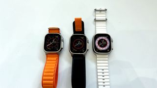 Tre stycken Apple Watch Ultra ligger bredvid varandra med olika armbandstyper och färger.