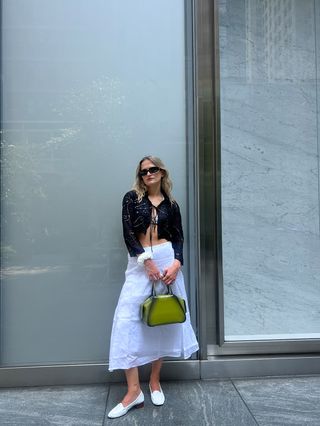 Eliza Huber wearing a black bolero, silver bikini top, white linen skirt, and white heeled loafers from the J.Crew x Maryam Nassir Zadeh collaboration.