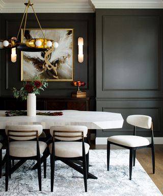 Dining table with upholstered chairs, floral arrangement and pendant light above in room with charcoal paneled walls