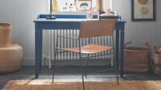 Blue desk with leather chair in front of white panelled wall with jute carpet, white radiator, lemon artwork, and mismatched storage baskets