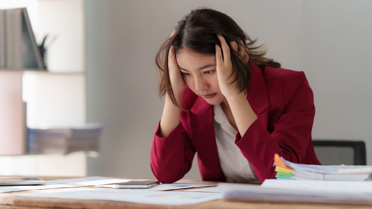 A woman stares at a stack of bills looking frustrated.