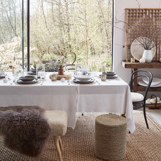 Dinner table set with white and grey dinnerware on top of rattan round placemats in front of large window