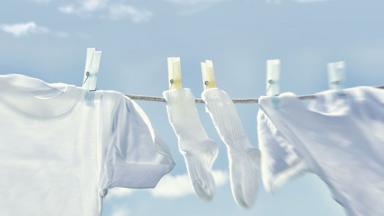 two white shirts and a pair of white socks hanging from a washing line with plastic pegs against a blue sky