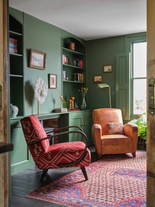 Green living room with built in shelving, armchairs and colorful vintage rug