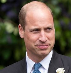 Prince William wearing a suit with a white flower and smiling in front of trees at the Duke of Westminster's 2024 wedding