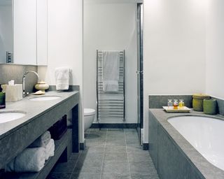 bathroom with towel storage below double sinks, toilet and towel rail