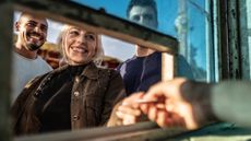 Three smiling young people buying tickets at a ticket booth window
