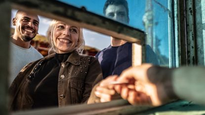 Three smiling young people buying tickets at a ticket booth window