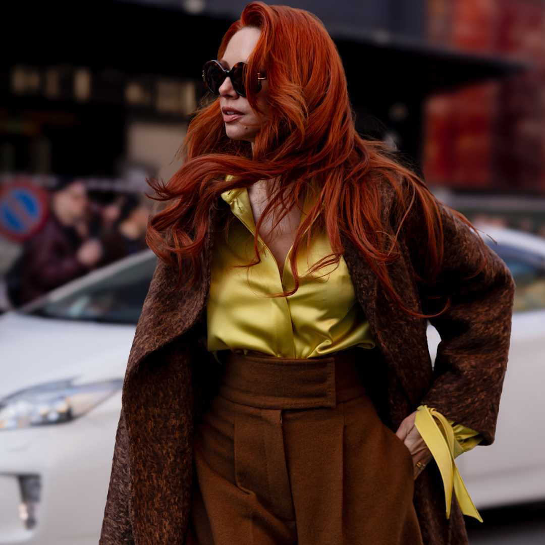 a fashion week attendee with red hair wears brown suit, green silk top, sunglasses