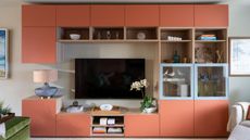 Living room with built-in cubby storage on the wall painted in Naperon by Farrow & Ball, a large TV mounted on the wall at the centre, and a lamp and orchid on either side.