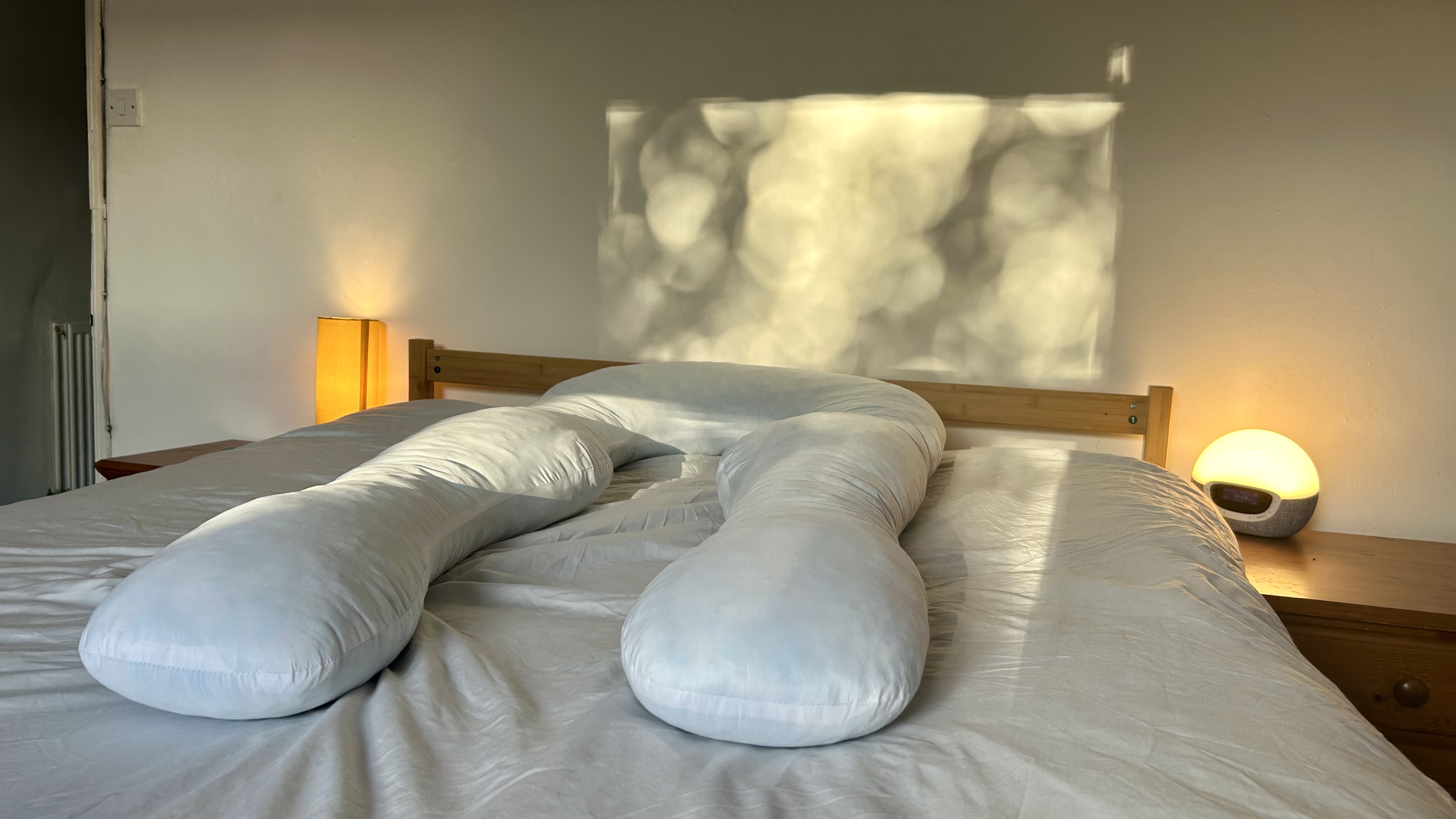 The Yana 360&amp;deg; Body Pillow laying on a bed dressed in white bedding, showing its ergonomic design.