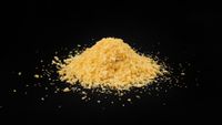 A pile of yellow bread crumbs sits against a black surface