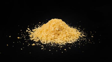 A pile of yellow bread crumbs sits against a black surface