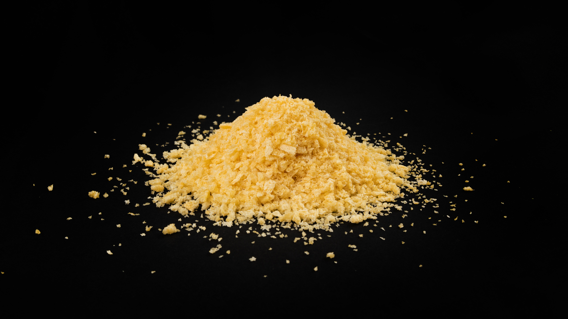 A pile of yellow bread crumbs sits against a black surface