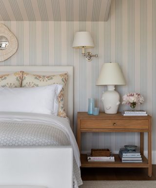 blue and white striped bedroom wallpaper with a white layered bed and wall and table lamp