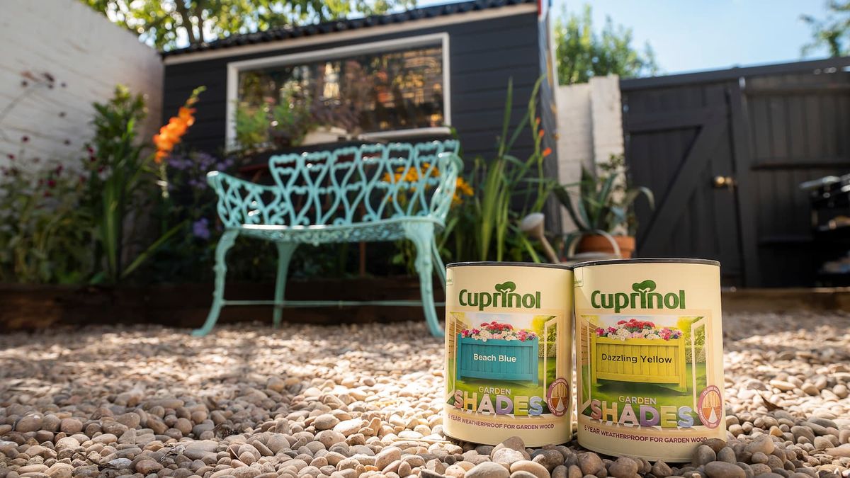 Two tins of Cuprinol paint in front of a grey shed