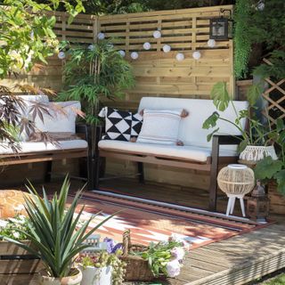 garden with wooden fencing, wooden decking with string lights and garden chairs