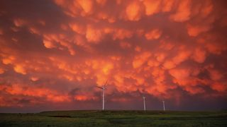 Vivid orange mammatus clouds over wind turbines on a green plain