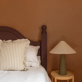 A bedroom with a brown-painted wall and a bed hearboard in a darker brown shade