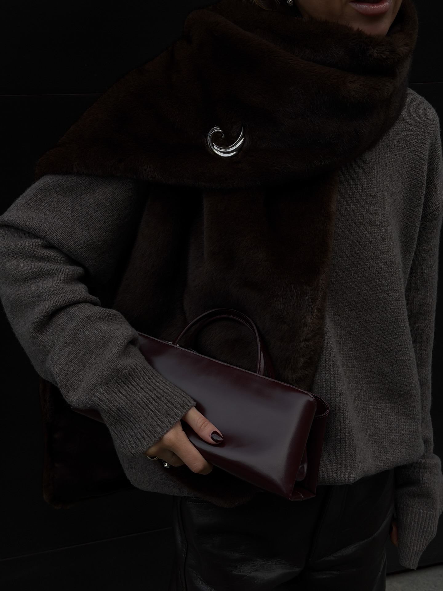 Woman wears a grey sweater, fur stole with silver pin and Verafied's eclair bag in burgundy.