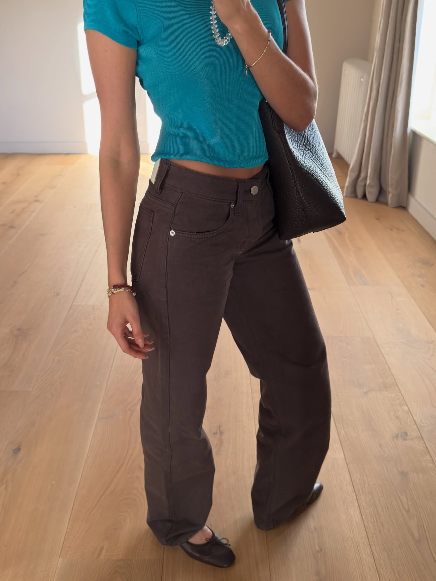 @smythsisters wearing a teal T-shirt, brown high-waisted jeans, and ballet flats.