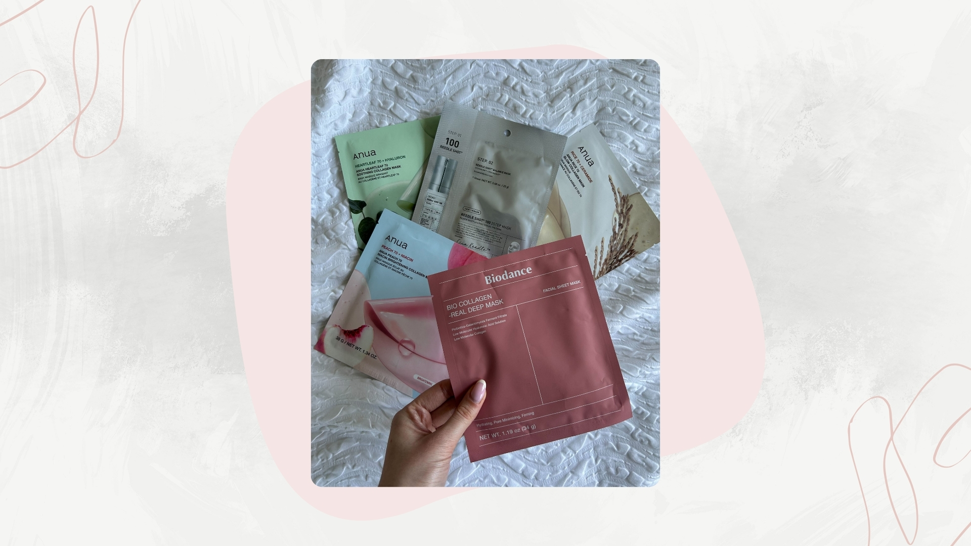 Image of Korean Face Masks on a white bed with hand holding the pink packet of Biodance face mask, on a white background with pink motifs and swirls