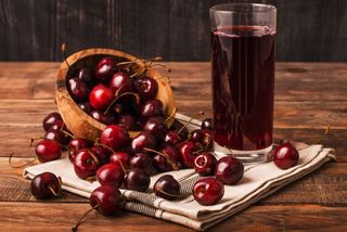 Cold cherry juice in a glass with ripe berries in bowl on a table