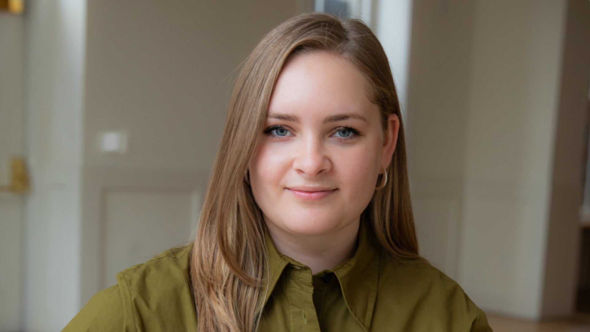A photo of Lisa Vedernikova Khanna, wearing a button-up olive-green shirt, smiling in an indoor setting.