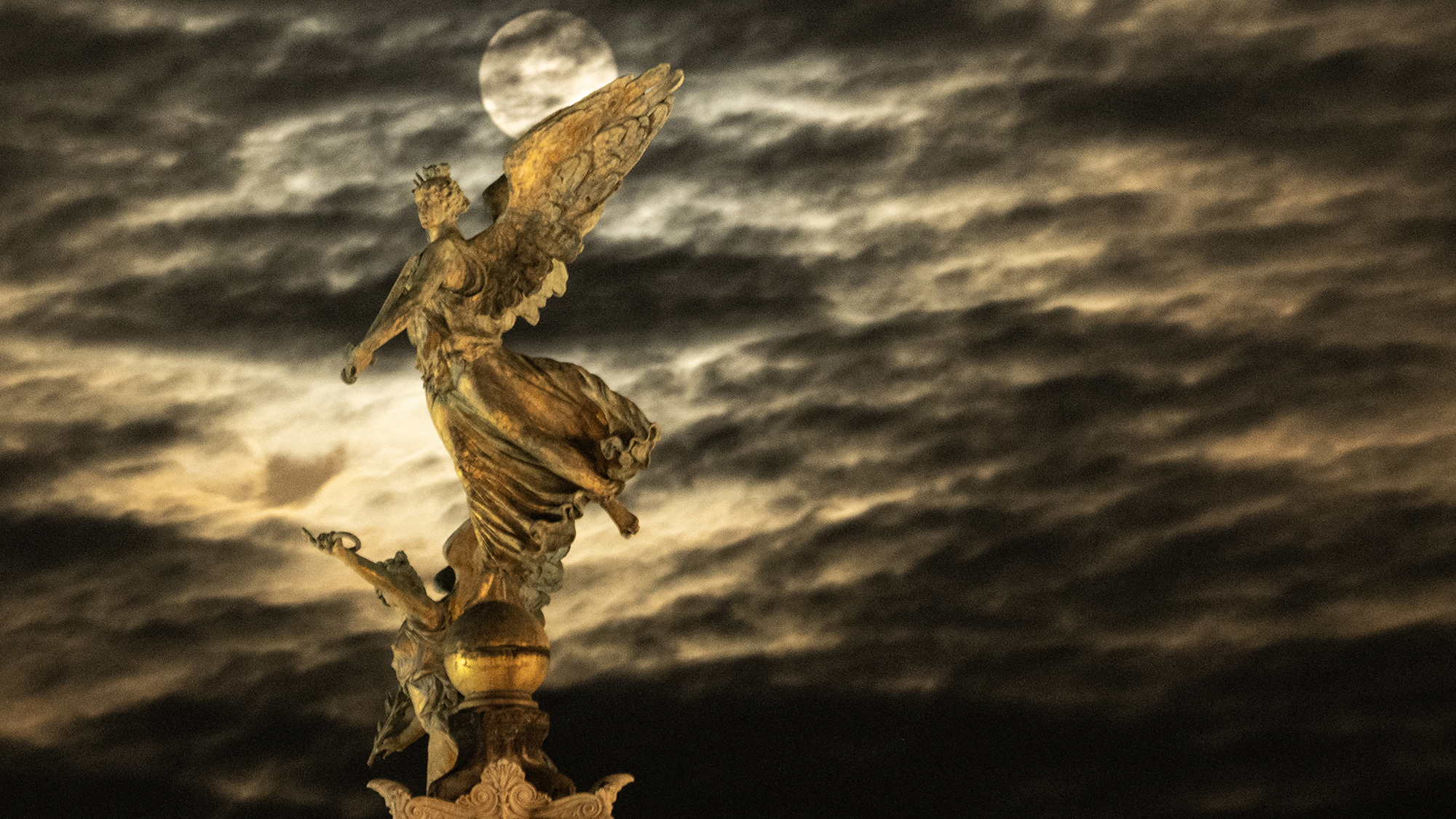 A full moon rises behind an angel statue on the top of a column at Piazza Venezia in Rome, Italy