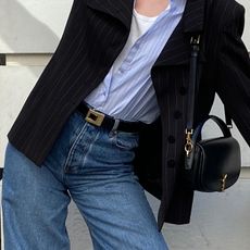 NYC woman wears a Saint Laurent black leather belt with gold hardware, black blazer, a blue button up and jeans. 