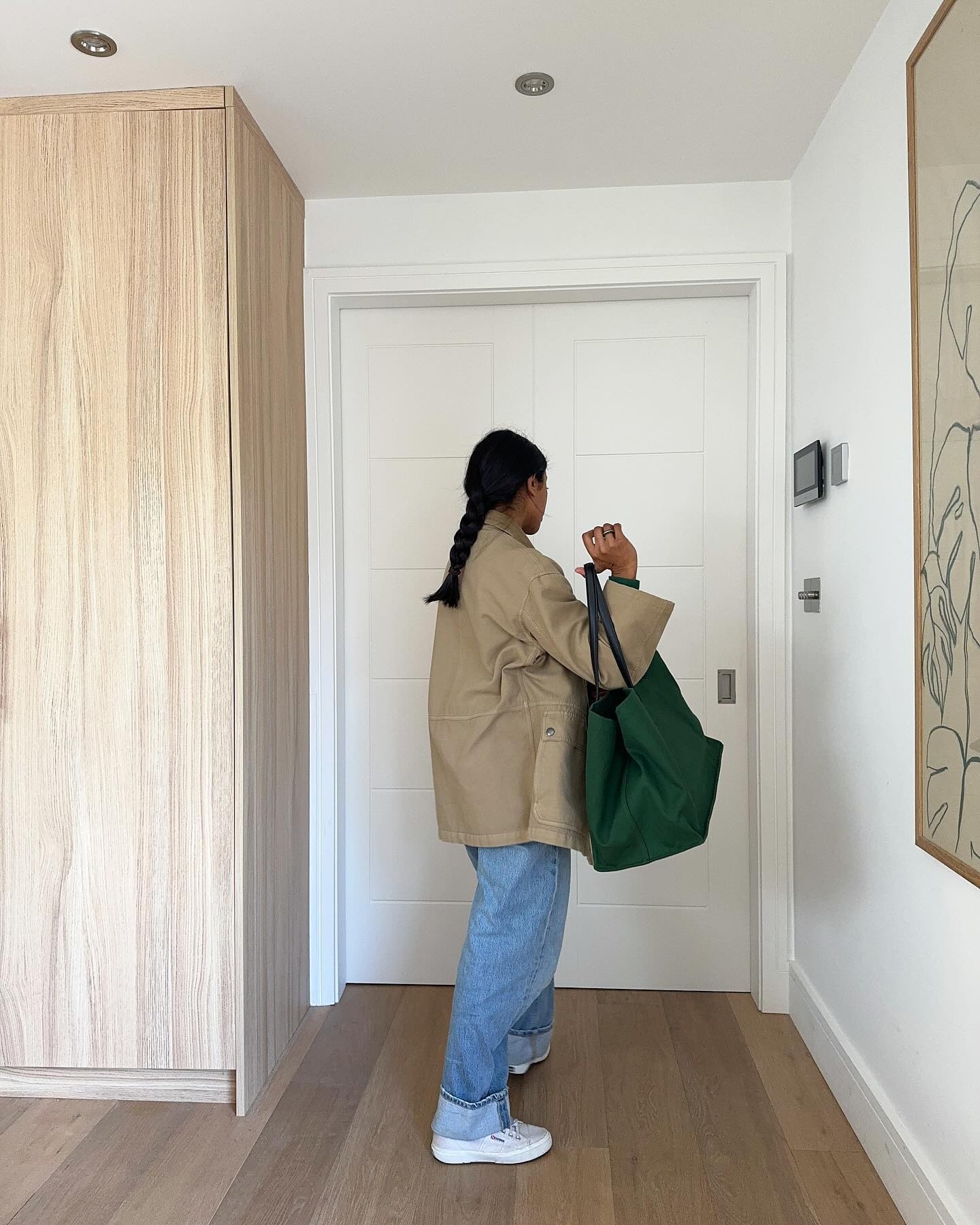 Monikh Dale wearing a tan jacket, jeans, and a green tote bag.