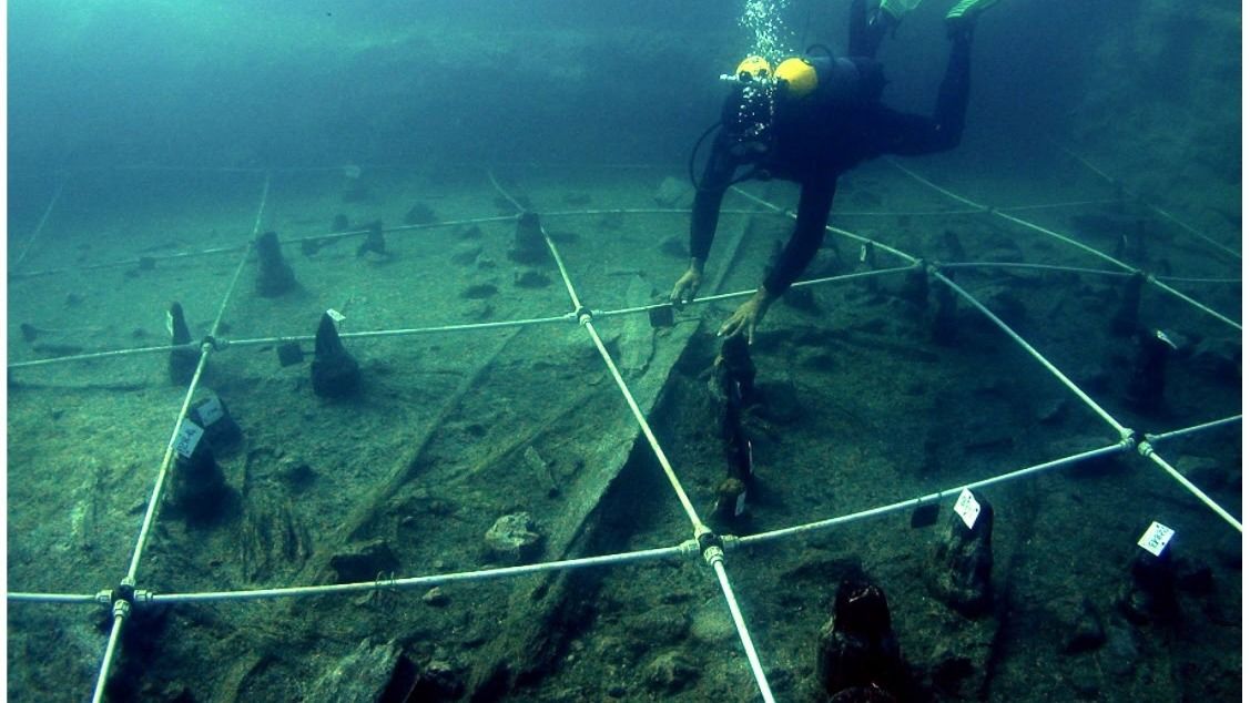 A scuba diver swimming toward a canoe underwater